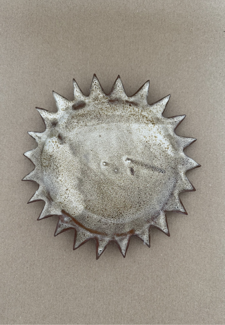 A ceramic plate with a spiked sunburst rim in a speckled glaze